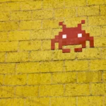 Red space invader alien on a yellow brick wall