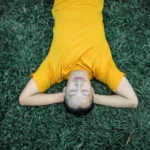 man lying on grass, content to procrastinate
