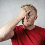 Man in red shirt holding his face