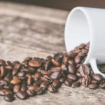 A white cup laying on the side with spilled coffee beans